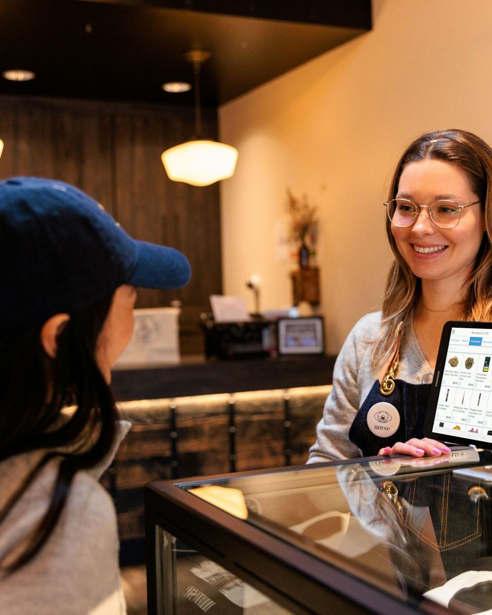 A shop assistant serving a customer at a counter, showing them a screen